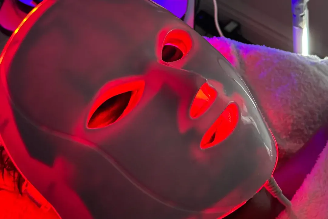An LED light therapy mask glowing red on a face